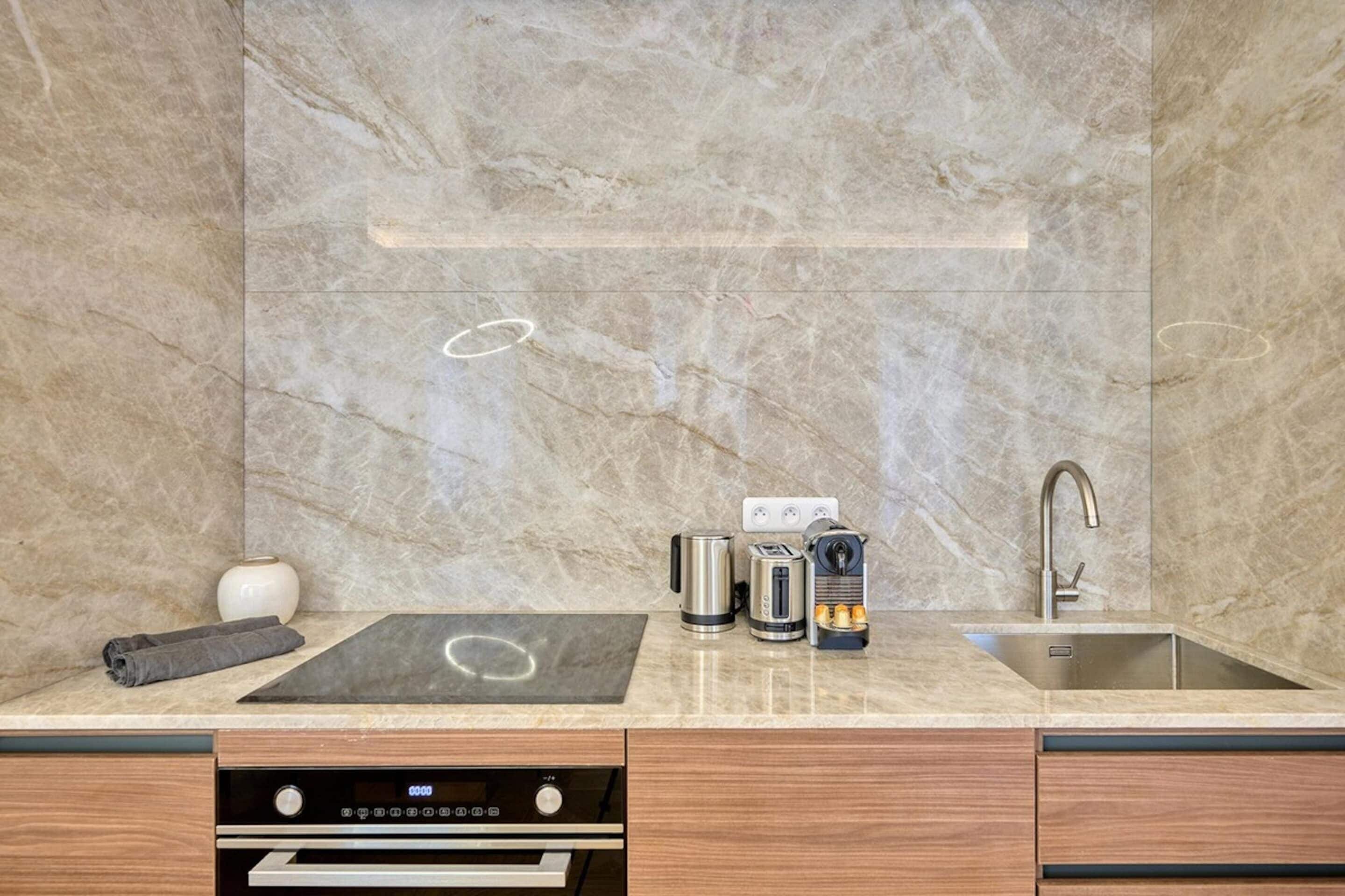 A modern kitchen with a marble backsplash, a built-in oven, a sink, and a coffee maker.