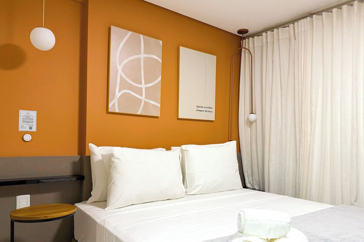Ein Hotelzimmer mit Bett, weißen Kissen, einem kleinen runden Tisch und einem Paar zusammengerollter Handtücher auf dem Bett.