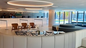 A modern reception area with a curved seating arrangement, a reception desk, and large windows offering views of the outdoors. - Paraíso no Porto Alto Resort (Ipojuca)