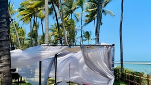 A beachside lounge with a canopy bed and two sun loungers, surrounded by palm trees and a clear view of the ocean. - Paraíso no Porto Alto Resort (Ipojuca)