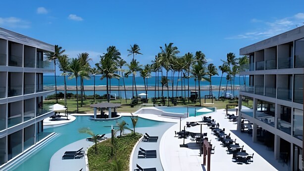 A resort pool with a view of the beach, palm trees, and modern buildings. - Paraíso no Porto Alto Resort (Ipojuca)