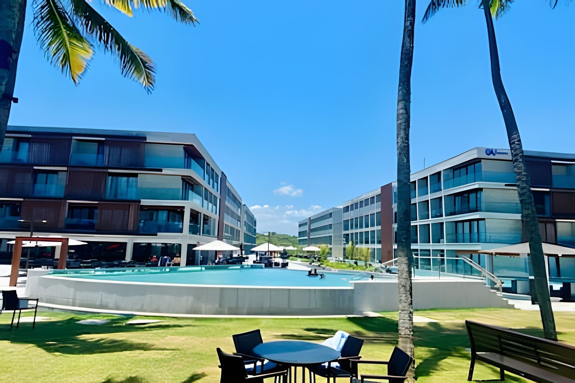 Un hôtel moderne doté d’une piscine centrale, d’un espace extérieur aménagé et de palmiers.