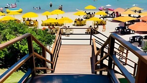 A wooden staircase leading to a beach area with yellow umbrellas and people. - Paraíso no Porto Alto Resort (Ipojuca)
