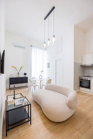 A modern living room with a curved sofa, a glass coffee table, and a dining area with a white table and chairs.