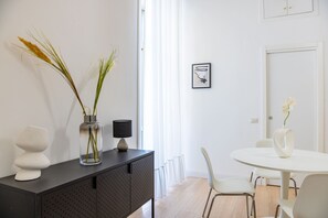 Uma sala de jantar moderna com uma mesa redonda, cadeiras brancas, um armário preto e um vaso com flores.