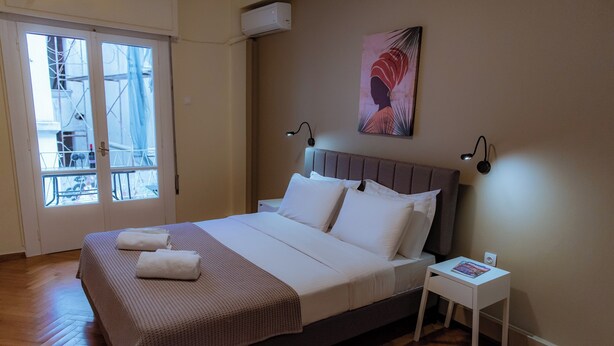 A neatly made bed with white linens and a brown blanket, a small bedside table with a magazine, and a wall-mounted artwork. - Plaka Apartment (Athens)
