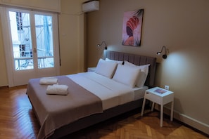 A neatly made bed with white linens and a brown blanket, a small bedside table with a magazine, and a wall-mounted artwork. - Plaka Apartment (Athens)