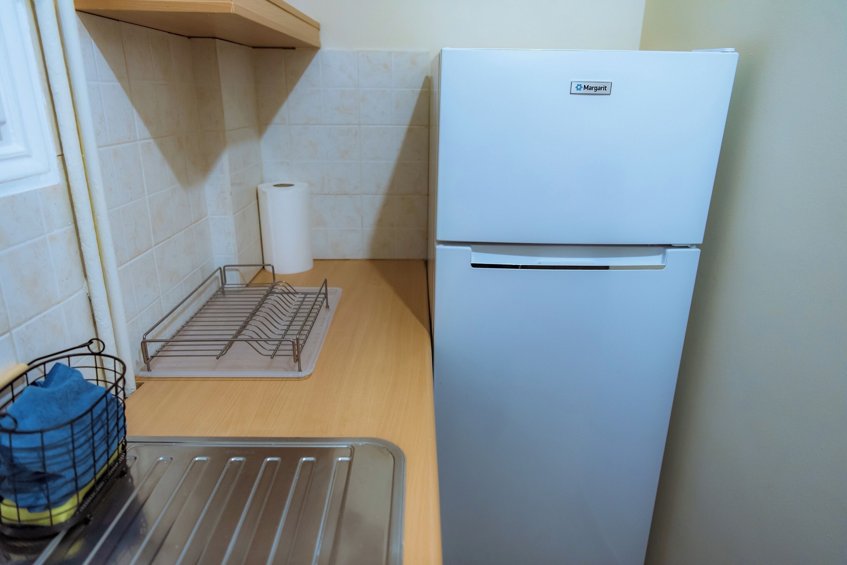 A compact kitchen with a white refrigerator, a metal drying rack, and a small metal tray.