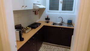 A compact kitchen with dark cabinets, a countertop, a sink, and a window with blinds. - Plaka Apartment (Athens)