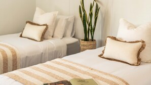 A hotel room with two beds, each with a striped blanket and a pillow. There is a potted plant on a side table.