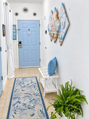 A hallway with a blue door, a white bench with a blue cushion, a patterned rug, and a wall-mounted plant. - Condo Magically close to Disney World- Easy Access to Universal- Serene Lakeview (Orlando)