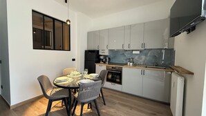 Cocina compacta con armarios grises, un refrigerador negro, horno empotrado y encimera de madera.
