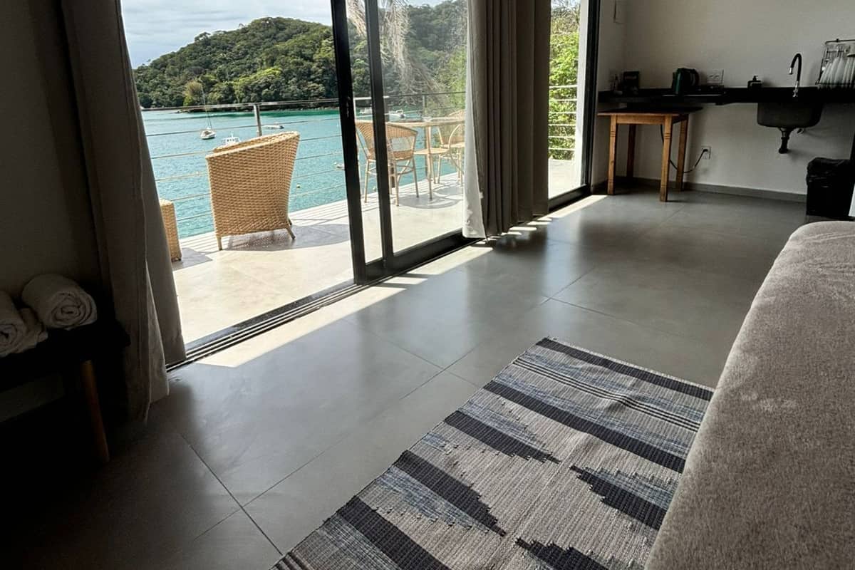 Una habitación de hotel moderna con un amplio ventanal corredera que da a un balcón con vistas al paisaje costero.