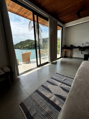 A modern hotel room with a large sliding glass door leading to a balcony with a view of a coastal landscape. - Flat Praia Comprida (Angra dos Reis)