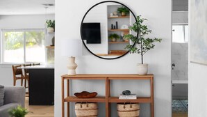 Een moderne woonkamer met een houten console, een ronde spiegel en een potplant.