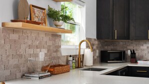Een moderne keuken met een wit aanrecht, een glazen schaal, een houten plankje met decoratieve objecten, en een donker kastje.