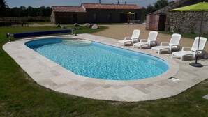 A swimming pool with a stone deck, surrounded by grass and a few lounge chairs. - 2-seater studio near Puy du Fou (Bressuire)