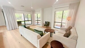 A spacious living room with large windows, a sofa set, a coffee table, and a chair.