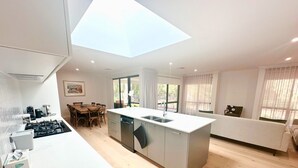 A modern kitchen with a central island, dining area, and a large skylight.