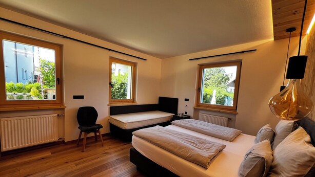 Una camera da letto moderna con due letti, ampie finestre, una poltrona e un termosifone.