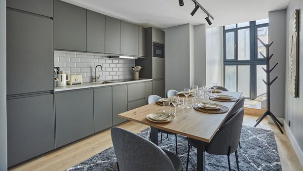 A modern kitchen with grey cabinets, a wooden dining table set for four, and a large window providing natural light. - Sublime and new Apartment Le Marais / Beaubourg (Paris)