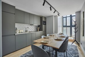 Een moderne keuken met grijze kastjes, een houten eettafel gedekt voor vier personen en een groot raam dat natuurlijk licht binnenlaat.