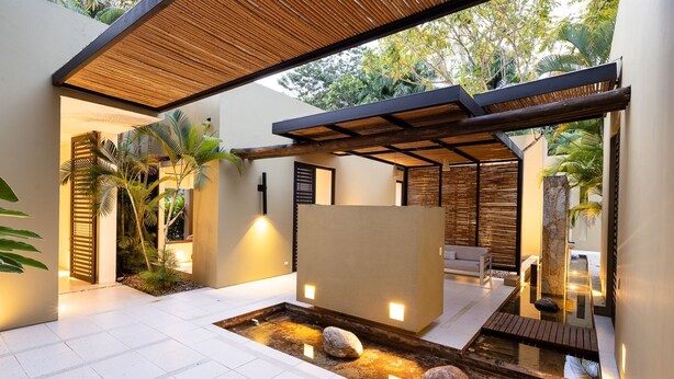 Un patio moderno al aire libre con fuente de agua, mobiliario y una pérgola de madera.