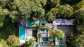 Vista aérea de un complejo turístico con varias edificaciones, una piscina y abundante vegetación que rodea la propiedad.