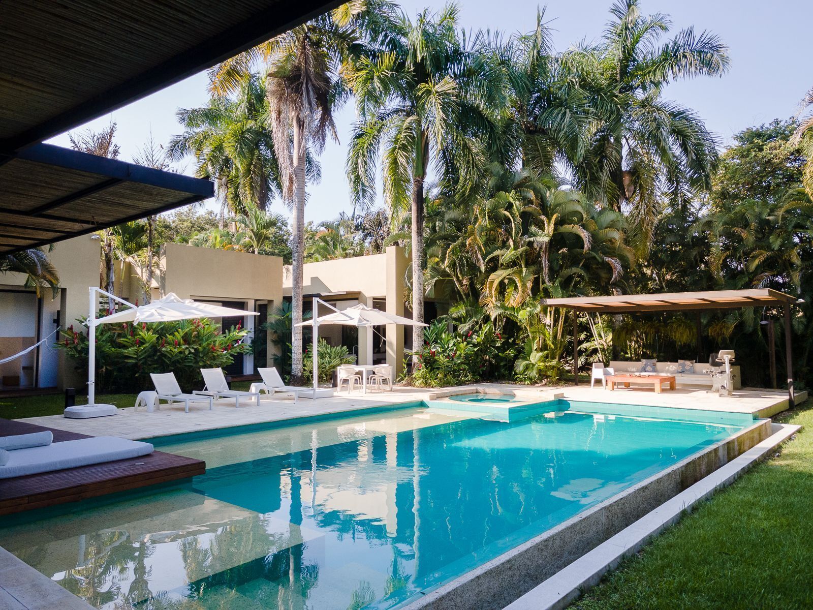 A swimming pool with lounge chairs and umbrellas, surrounded by palm trees and greenery.