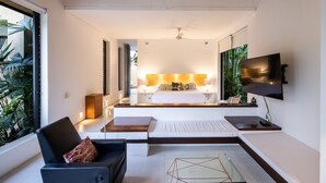 Habitación de hotel moderna con una cama grande, un televisor montado en la pared y una zona de estar con una mesa de vidrio.