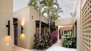 Un espacio exterior moderno con un camino, palmeras y un edificio de fachada clara y detalles negros.