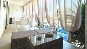 Una habitación moderna y luminosa con una mesa de centro de vidrio, muebles blancos y cortinas de gasa.