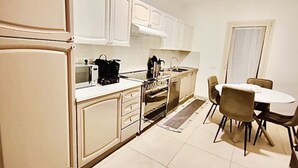 Una cocina compacta con armarios blancos, estufa, microondas y una zona de comedor con mesa y sillas.