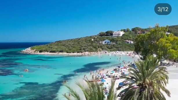 Una playa con aguas turquesas cristalinas, palmeras y una multitud de gente.