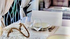Un comedor con una mesa preparada para dos, con platos blancos, copas de vino transparentes y un objeto esférico blanco decorativo.