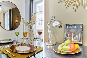 A dining area with a table set for two, a mirror, a vase with flowers, and a framed picture on the wall.