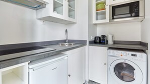 A compact kitchen with white cabinets, a built-in microwave, a washing machine, and a sink.