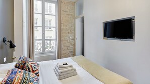 Camera d'albergo con un letto, una finestra con tende, un muro in pietra, una TV a parete e una lampada.