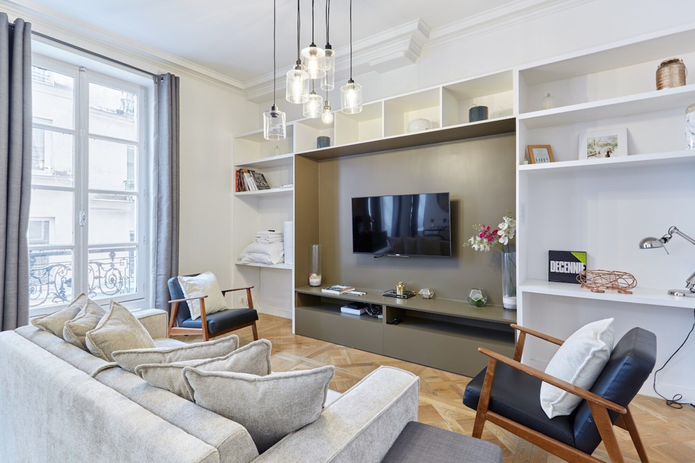 Una sala de estar moderna con un sofá gris, una silla de madera, un televisor de pantalla plana y una estantería.