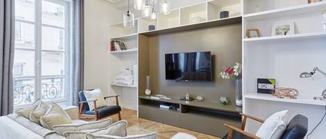 Una sala de estar moderna con un sofá gris, una silla de madera, un televisor de pantalla plana y una estantería.