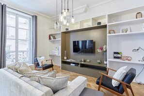 A modern living room with a grey sofa, a wooden chair, a flat-screen TV, and a bookshelf. - Superb Apartment Le Marais Center of Paris (Paris)