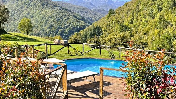 A swimming pool with a wooden deck and lounge chairs, surrounded by lush greenery and mountains in the background. - New! Restored farmhouse,private pool,plunge pool, river! Walk pizzeria. Perfect! (Toscana)