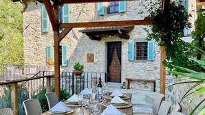 An outdoor dining area with a stone building in the background, a wooden pergola, and a table set for four with chairs. - New! Restored farmhouse,private pool,plunge pool, river! Walk pizzeria. Perfect! (Toscana)