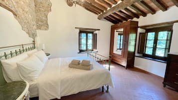 A bedroom with a large bed, wooden beams, stone wall, and windows.