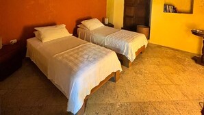 Une chambre avec deux lits, un ventilateur de plafond, une lampe fixée au mur et une porte.