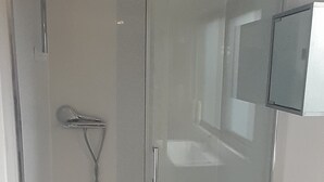 Eine begehbare Dusche mit Glastrennwand, einer Handbrause, einem weißen Waschbecken und einem Spiegel an der Wand.