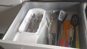Eine Schublade mit verschiedenen Küchenutensilien, darunter Löffel, Gabeln, Messer und Pfannenwender.