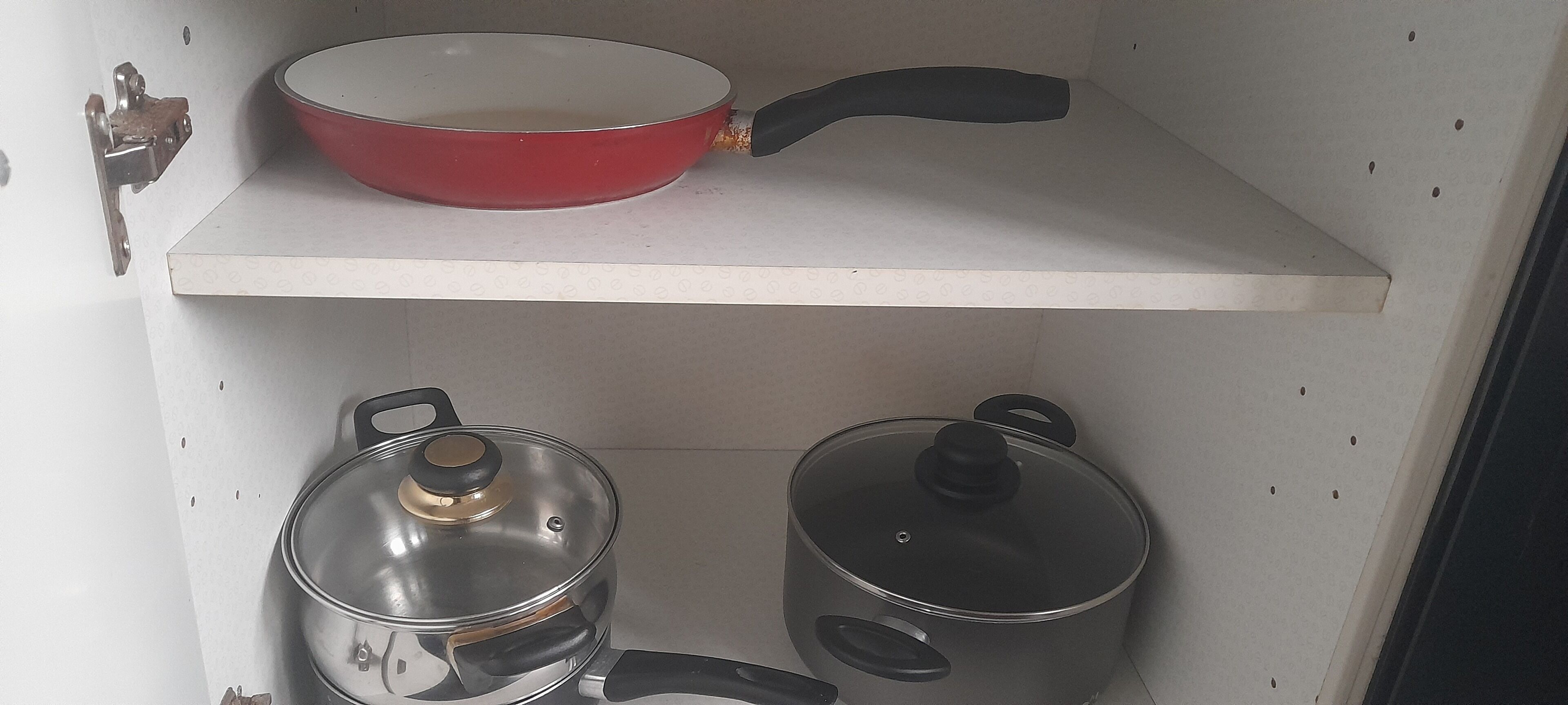 A kitchen shelf with a red frying pan, a stainless steel pot with a lid, and a pot with a lid.