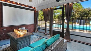 A screened-in patio with a ceiling fan, a projector, and a sign reading "Beach House." - Private spacious resort, jumbo heated salt water pool/spa, game room, office (Navarre)