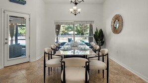 A dining area with a large table, chairs, a chandelier, a large mirror, and a view of the outdoors. - Private spacious resort, jumbo heated salt water pool/spa, game room, office (Navarre)